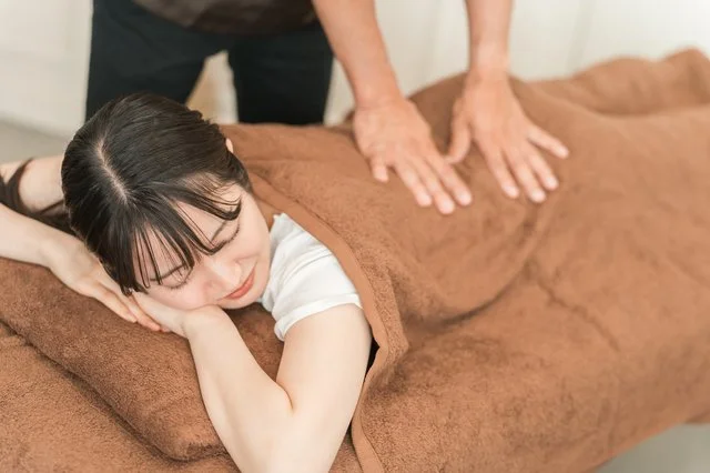 うつ伏せの方の背中から腰へ手のひらで圧をかけていくもみほぐしの施術